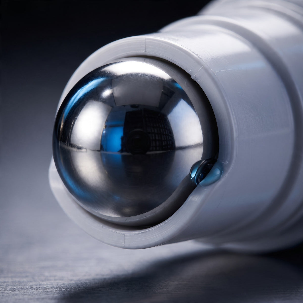 Close-up of a white cylindrical device with a polished metallic spherical roller on a dark gray surface. A white cylindrical skincare serum bottle with a metallic silver rollerball applicator cap, featuring the brand name 'STELLAR' printed vertically in blue on the front, set against a plain white background. By Skin-rg the ultiamte line and wrinkle relaxer.