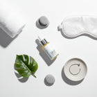 Skincare products including Skin-rg De Age Neck And Jowl Treatment dropper bottle, eye mask, and leaf on a white surface.
