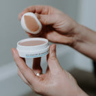 White jar with Pure Shield SPF 30 Adaptive Skin Tint with 'SKIN-RG' branding and words Pure Shield held in hands with applicator showing colour and texture of product. 